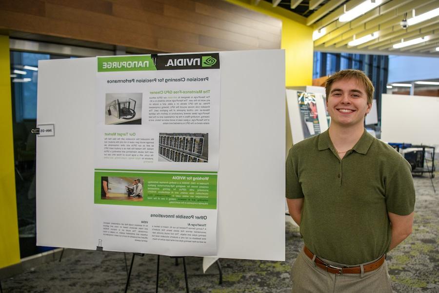 A male student smiles while standing in front of a poster describing a project.